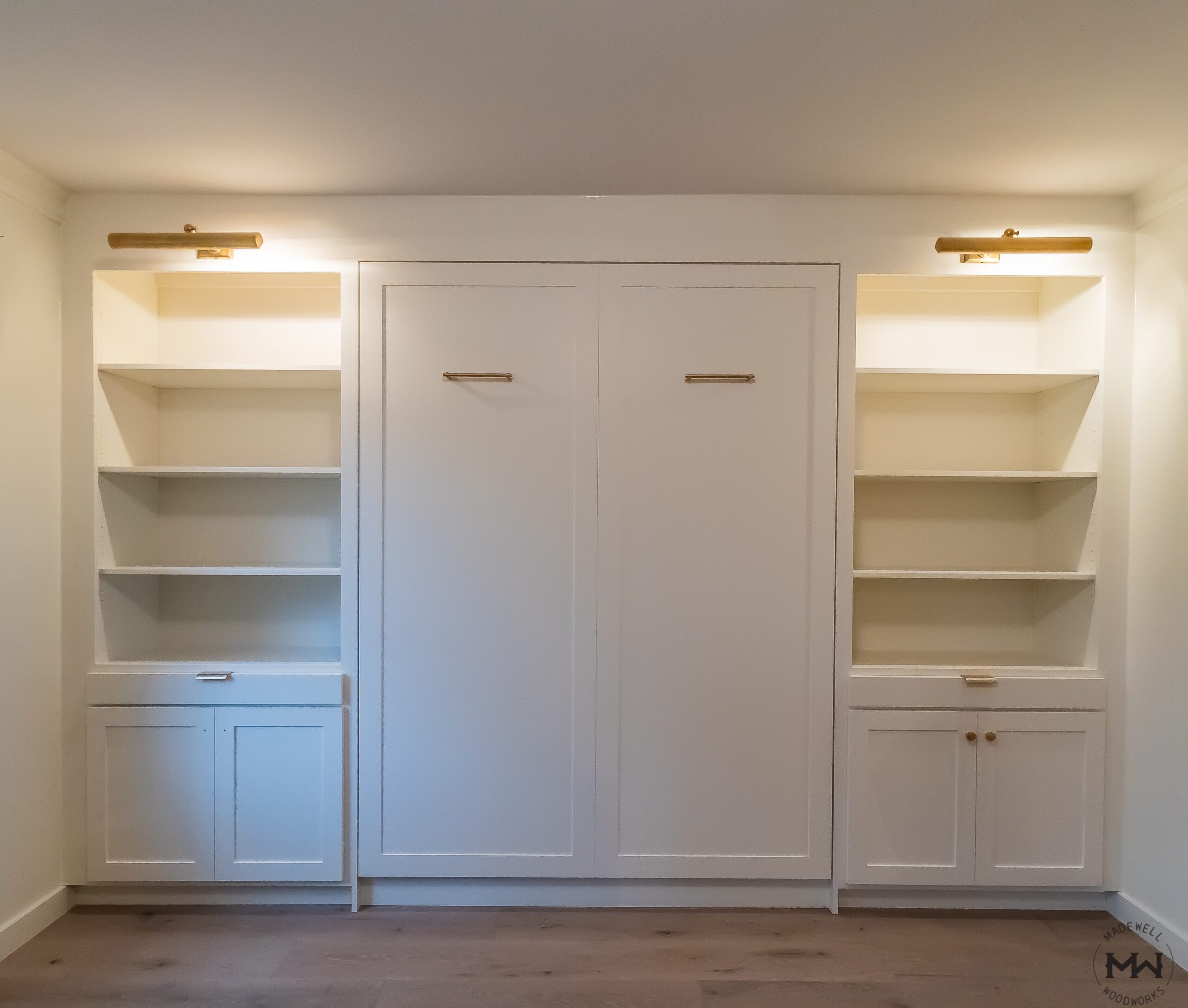Queen vertical Rivington Murphy bed with flanking open shelving towers and lower cabinets, painted white with brass hardware and cabinet lighting, Austin TX