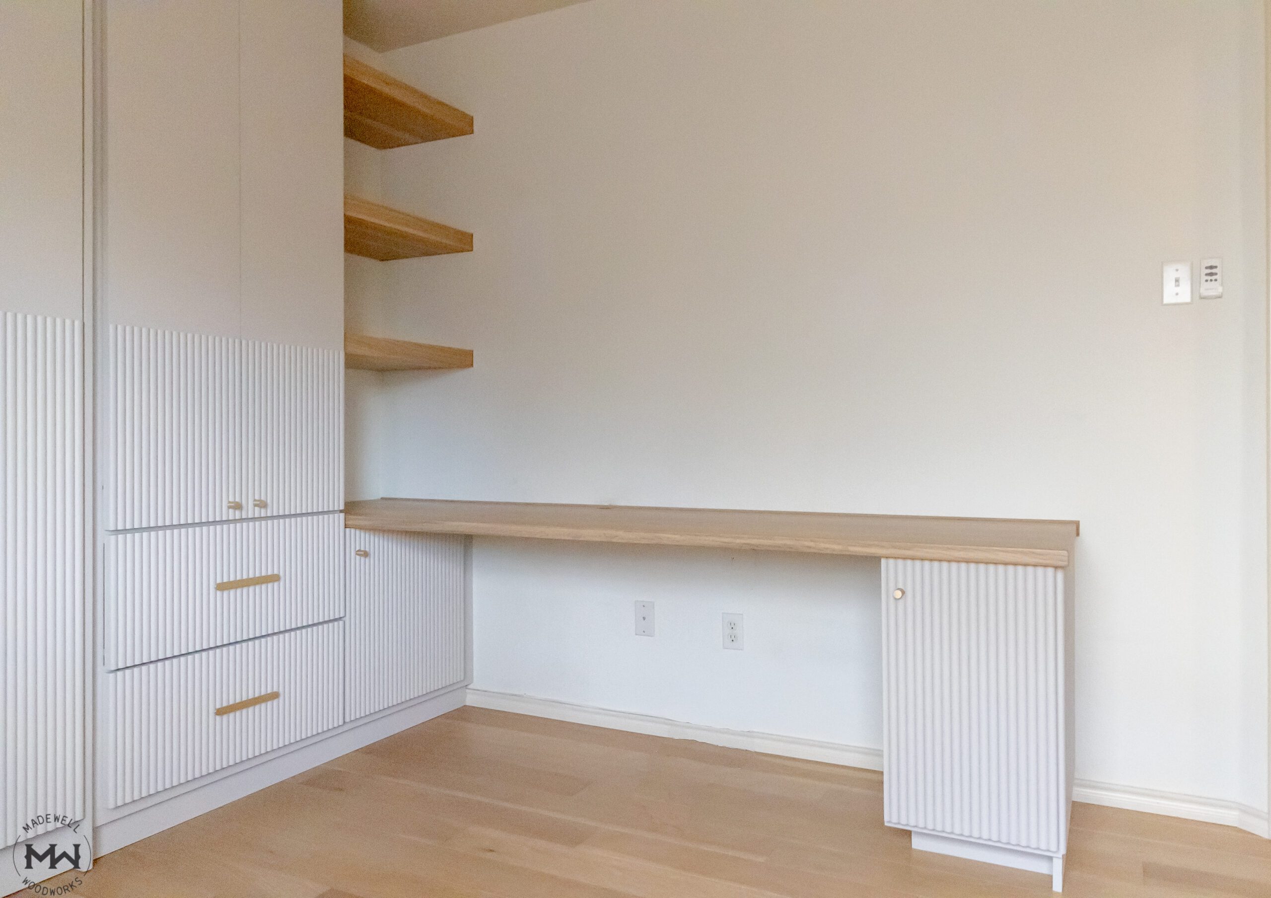 White fluted built-in cabinetry with floating wood desk, gold pulls, and open shelving