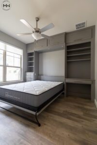 Custom-built gray queen Murphy bed with gold handles, integrated into a multifunctional wall unit featuring built-in shelving, drawers, overhead cabinets, and a compact desk. Features a open bed with a 12" Lull Premium mattress.
