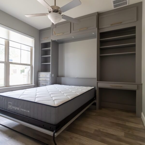 Custom-built gray queen Murphy bed with gold handles, integrated into a multifunctional wall unit featuring built-in shelving, drawers, overhead cabinets, and a compact desk. Features a open bed with a 12