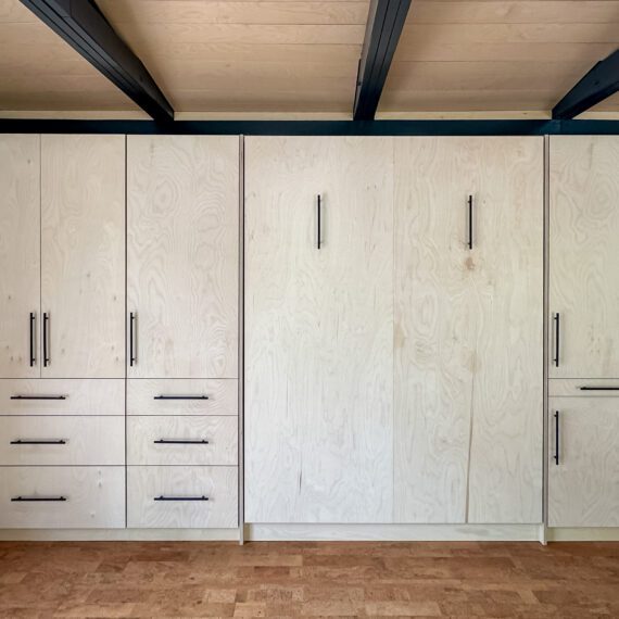 Front view of Baltic birch Murphy bed with black hardware and built-in cabinetry, handcrafted by Madewell Woodworks in Austin, Texas.