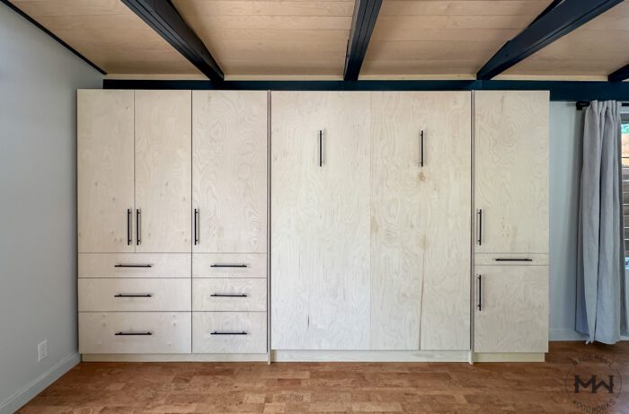 Front view of Baltic birch Murphy bed with black hardware and built-in cabinetry, handcrafted by Madewell Woodworks in Austin, Texas.