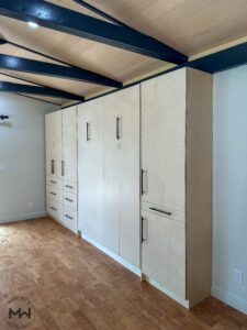Angled view of Baltic birch Murphy bed with black hardware and built-in cabinetry, handcrafted by Madewell Woodworks in Austin, Texas.