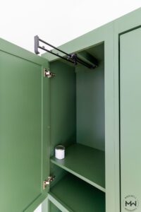 Close-up of a built-in wardrobe cabinet with a pull-out hanging rod, painted green and custom-built by Madewell Woodworks in Austin, Texas.