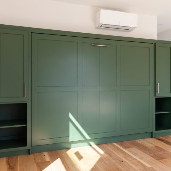 Queen-size horizontal Murphy bed in green shaker-style cabinetry with open shelving, handcrafted by Madewell Woodworks in Austin, Texas.