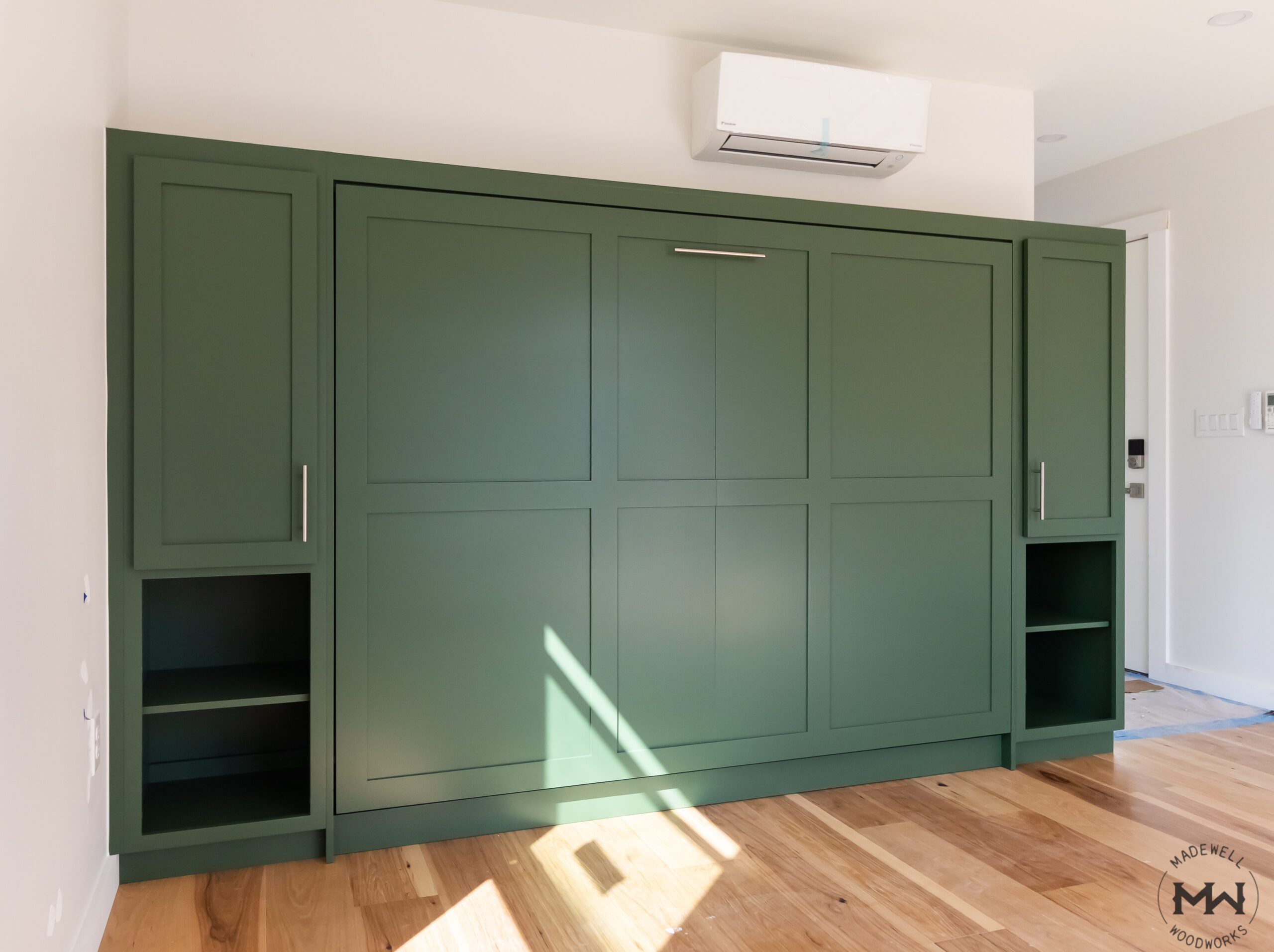 Queen-size horizontal Murphy bed in green shaker-style cabinetry with open shelving, handcrafted by Madewell Woodworks in Austin, Texas.