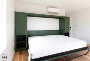 Queen-size horizontal Murphy bed in green shaker-style cabinetry with open shelving and a minimalist design, handcrafted by Madewell Woodworks in Austin, Texas.