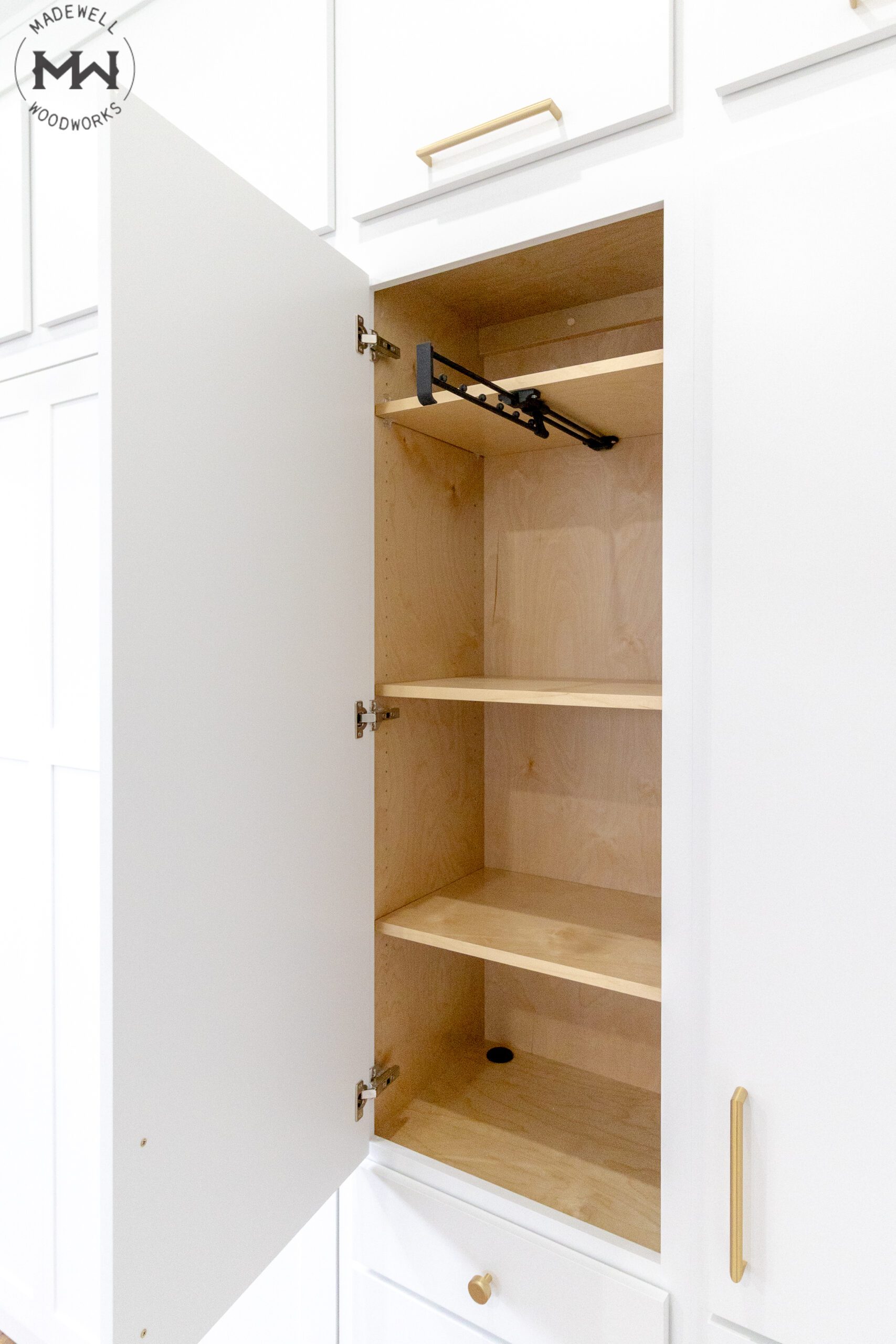 Interior cabinet detail of white Craftsman Murphy bed with maple shelving, gold hardware, and pull-out hanging rod, handcrafted by Madewell Woodworks in Austin, Texas.