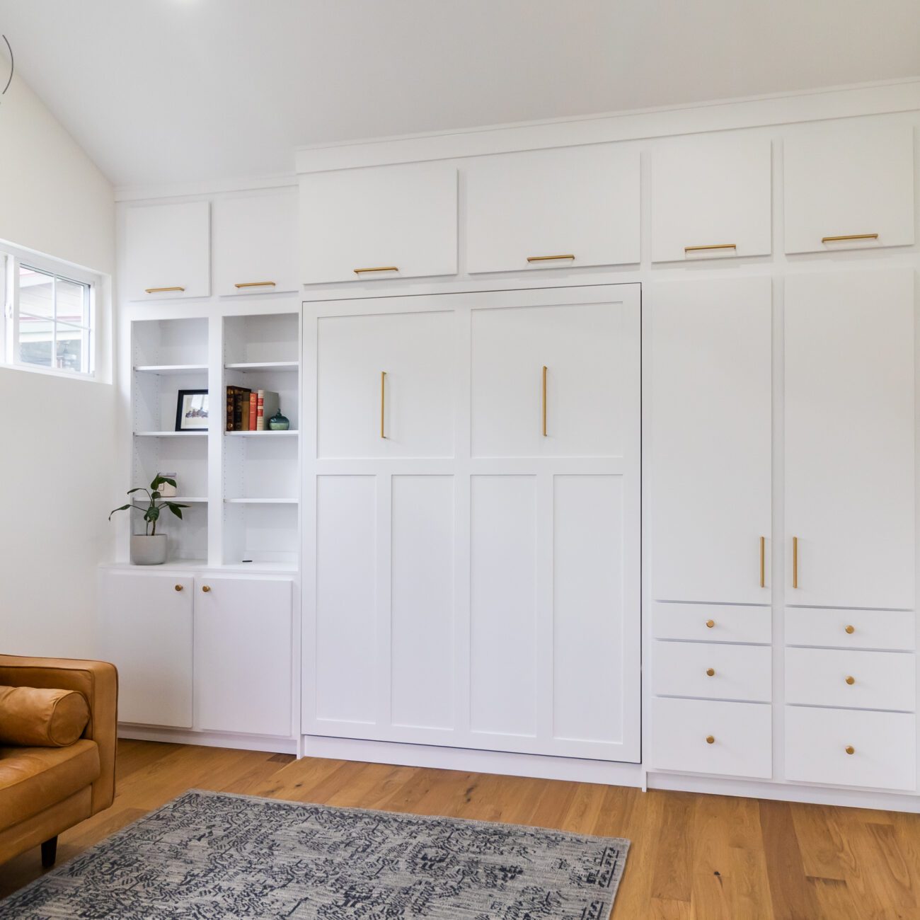 White Craftsman queen Murphy bed with gold hardware, built-in cabinetry, and upper storage, handcrafted by Madewell Woodworks in Austin, Texas.