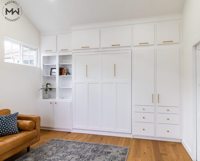 White Craftsman queen Murphy bed with gold hardware, built-in cabinetry, and upper storage, handcrafted by Madewell Woodworks in Austin, Texas.