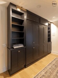 Side view of custom black Murphy bed with built-in shelving, record player nook, and museum-style lighting.