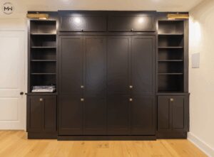 Custom black king Murphy bed with museum-style lighting, built-in shelving, and upper cabinetry.
