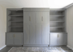Gray Murphy bed with shaker-style doors, brass handles, and built-in shelving.