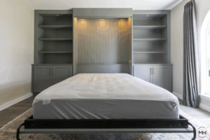 Gray Murphy bed with lighted beadboard backing and built-in shelving on both sides.