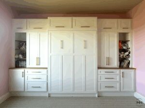 Custom white Craftsman-style Murphy bed with natural wood top, built-in cabinetry, and brass hardware, handcrafted in Austin by Madewell Woodworks.