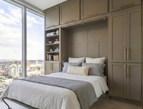 Custom Vertical Murphy Bed Open - Madewell Woodworks A custom vertical Murphy bed pulled down into a modern bedroom, featuring taupe cabinetry, gold hardware, and a large window view.