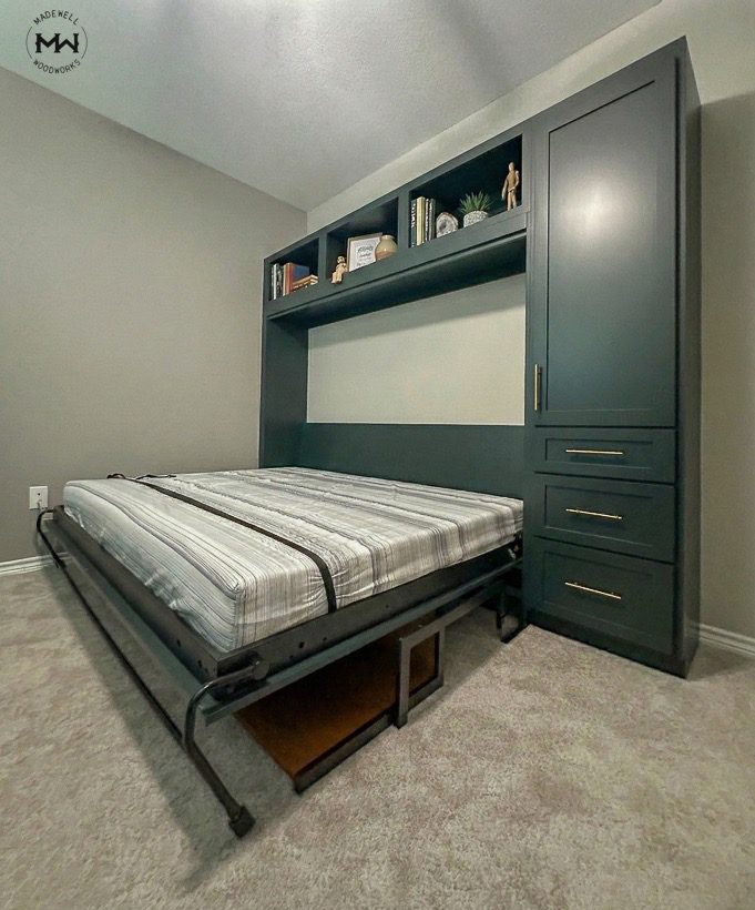 A side-mount horizontal Murphy bed in deep green, shown open with a white mattress and custom built-in shelving.