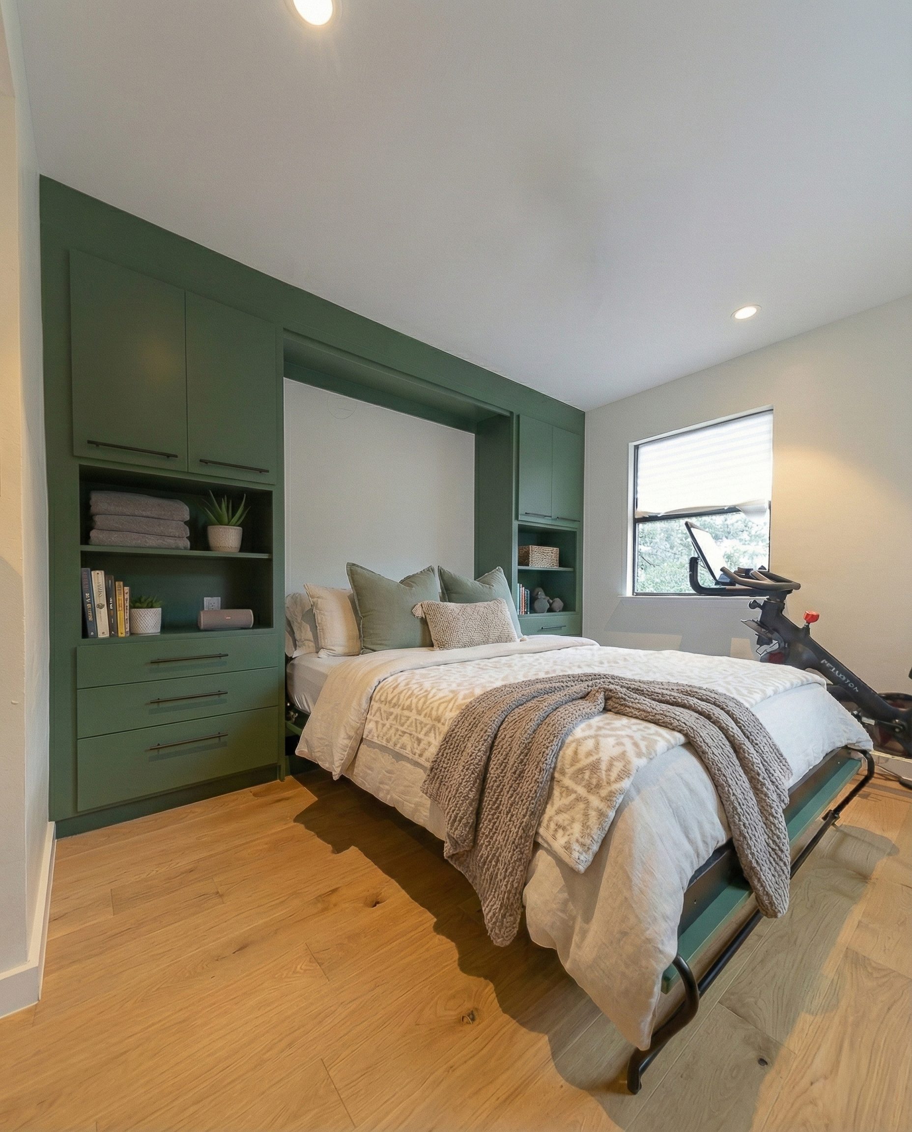 Queen vertical Murphy bed deployed in home gym, Martha's Vineyard green finish with open shelving and drawer bases, West Lake Hills TX