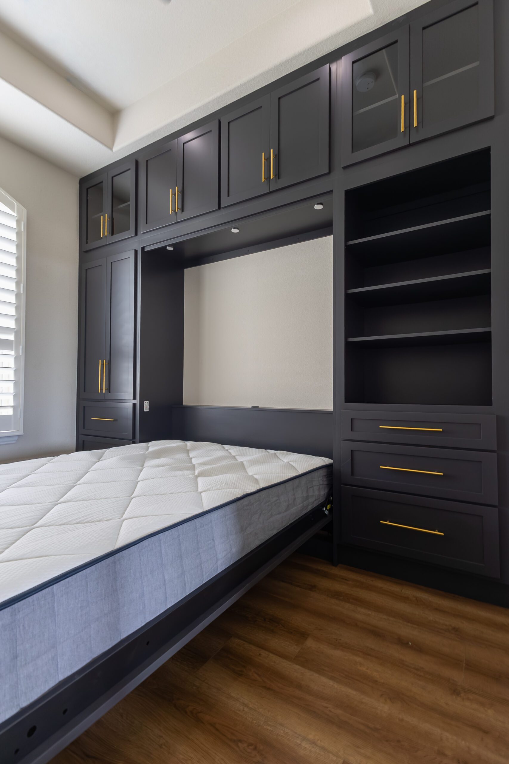 Black Murphy bed open with mattress deployed, built-in cabinets with gold handles and open shelving in Austin, TX