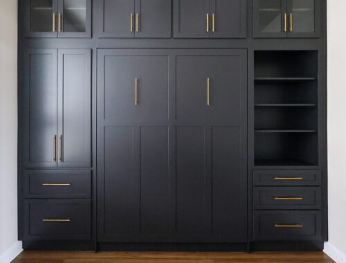 Built-in black cabinets with glass-front doors and gold handles, spanning wall, with open shelving on the right and drawers below.